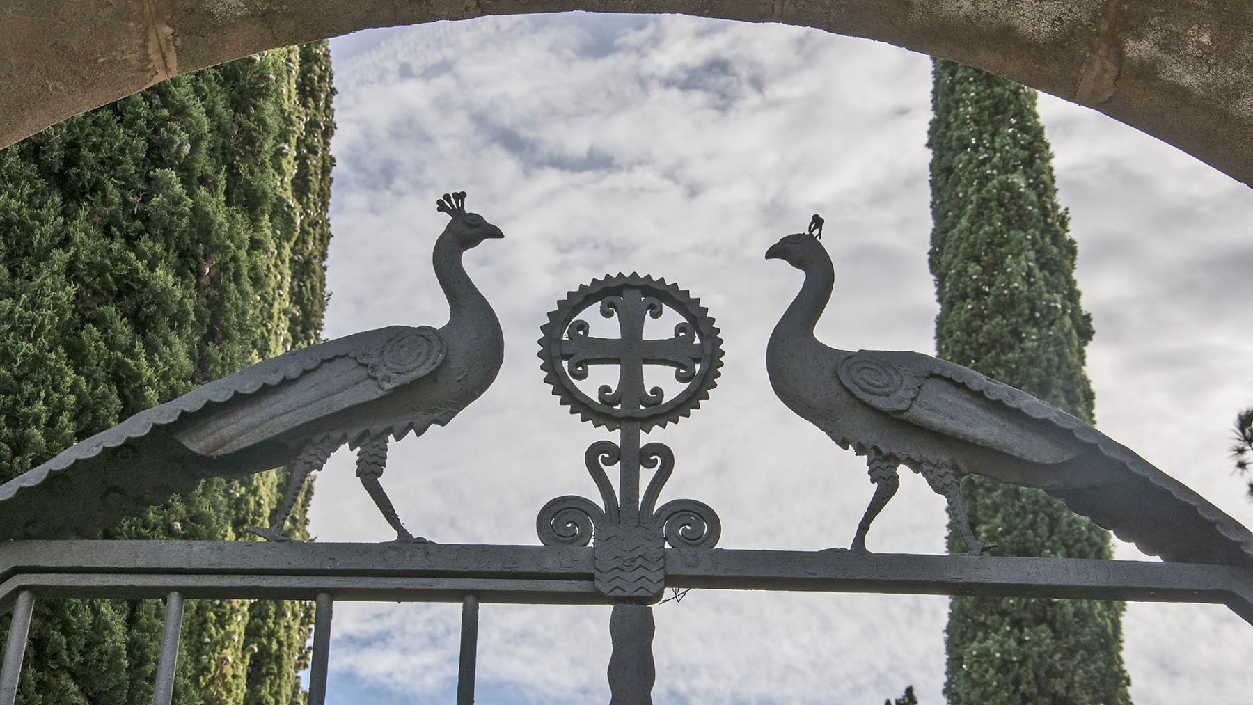 Llinda de la porta d'accés al cementiri amb un treball en forja que representen dos paons blaus, símbol cristià de la vida eterna